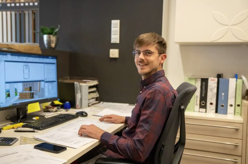 Thomas Zitz, Mitarbeiter bei Neubauer Küchen in Leibnitz sitzt vor seinem Computer im Büro und lächelt in die Kamera