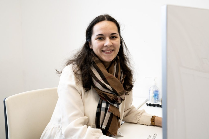 Anna-Maria Sommer sitzt mit weißer Bluse und gestreiftem Schal vor dem PC 