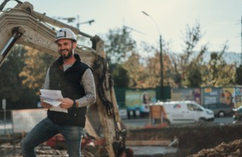Christopher Rothmann steht mit einem Plan in der Hand und einem Arbeitsschutzhelm auf einer Partl Bau Baustelle
