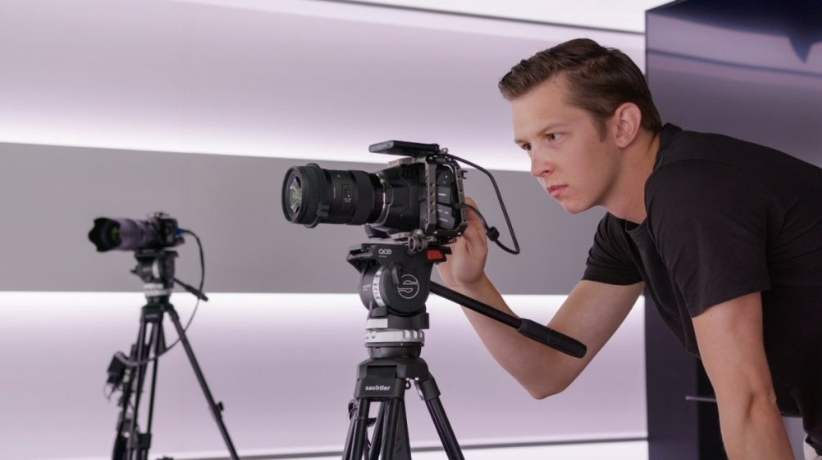Michael Ernst mit schwarzem T-Shirt schaut in eine Kamera die auf einem Stativ montiert ist. Dahinter eine zweite Kamera